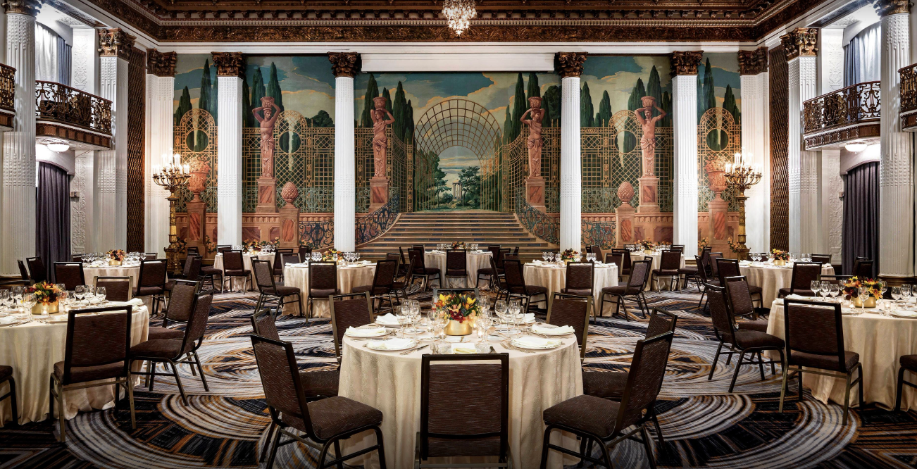 A ornate neoclassical ballroom with soaring pillars and a mural is set for a dinner party in San Francisco's National Register listed landmark historic luxury hotel.